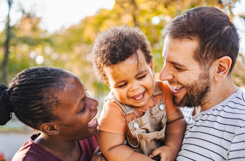 Mum and dad holding their child in between them, all are smiling