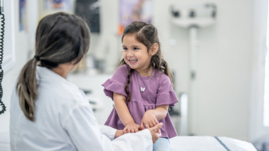 A young girl sitting opposite a female health professional, smiling, in what looks like a hospital/GP surgery.