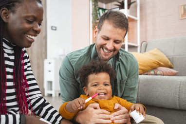 Man sat on floor holding early years child with woman smiling  