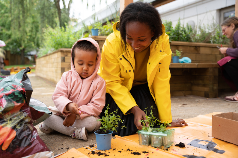 Woman and young child with pink hooded anorak potting plants outside