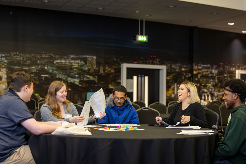 Four young people and an adult sat around a table laughing