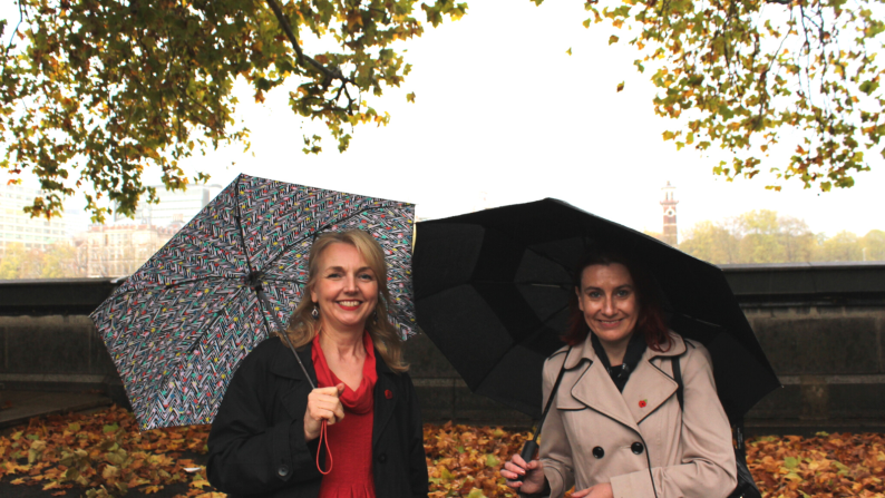 Two ladies smiling at the camera holding umbrellas outside of parliament