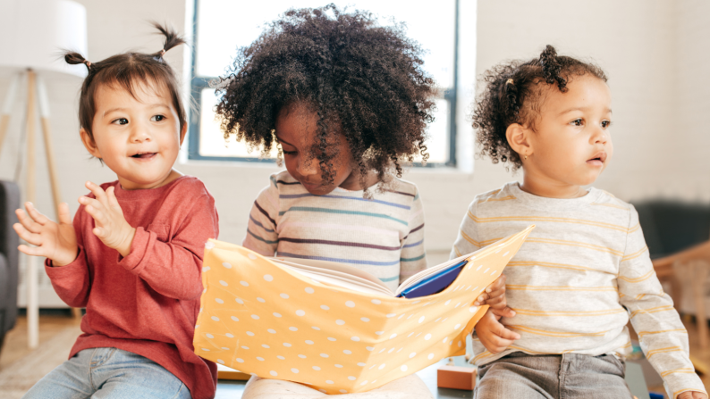 Three early years children with middle one holding a book
