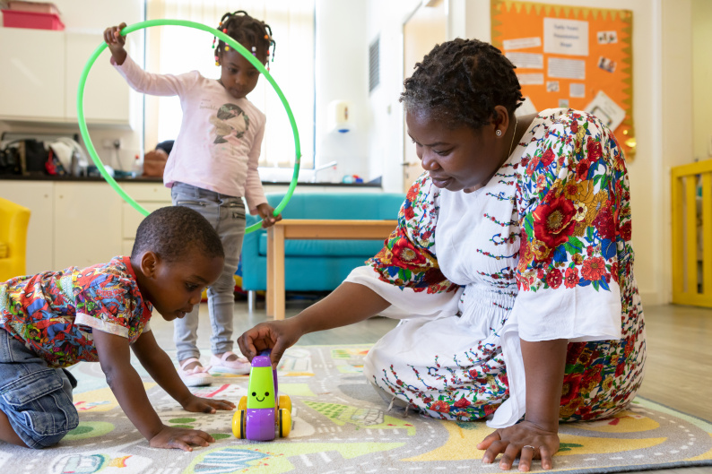 A woman playing with an early years child while an older child looks on