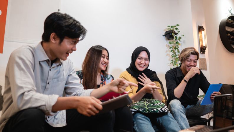 Gruop of four young people sat on a sofa talking and laughing.