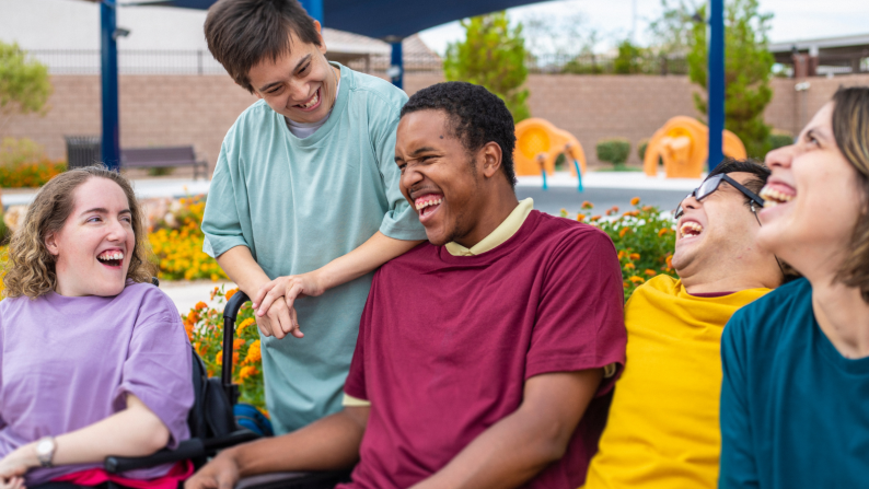 Group of young people sat on bench outside laughing