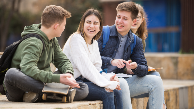 Group of young people sat on a wall talking and laughing