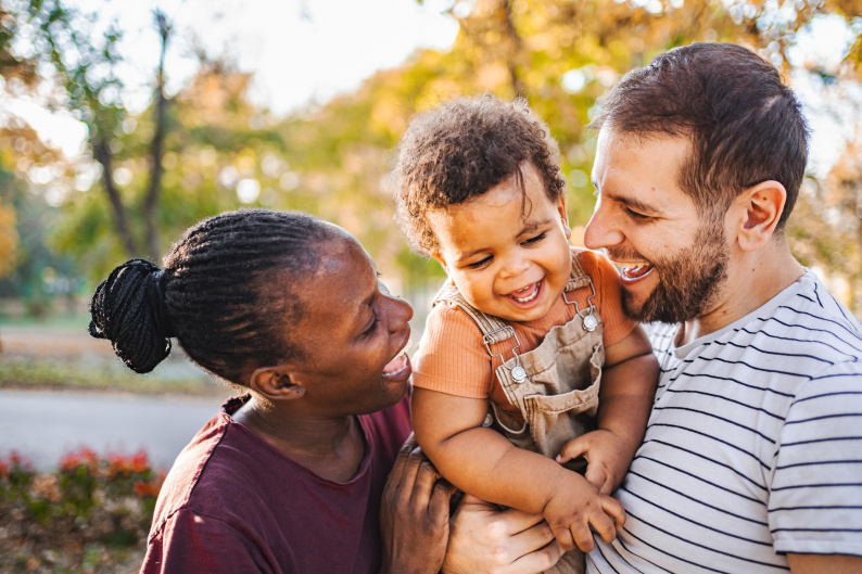 Smiling parents standing outside holding a child who is also smiling