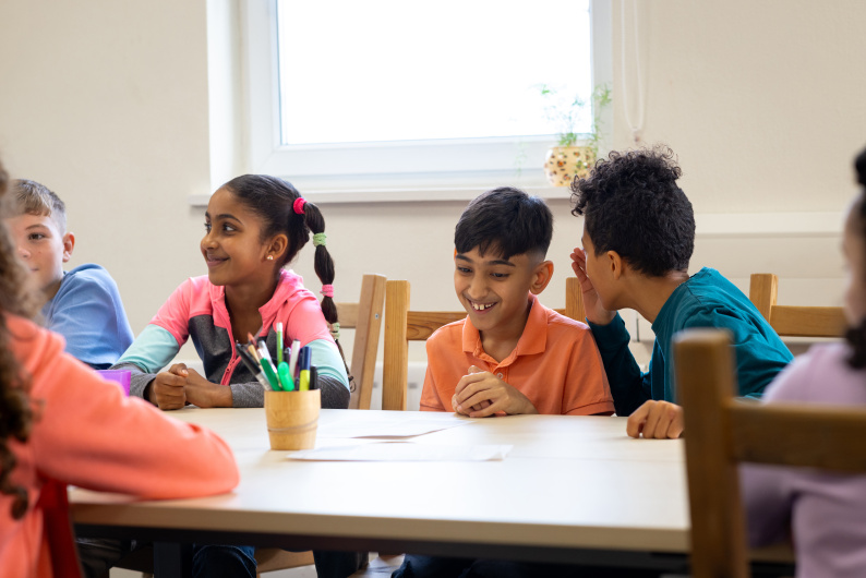 Two boys share a joke at a table with other children