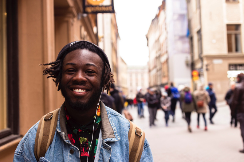 A young man on a street smiles into the camera.